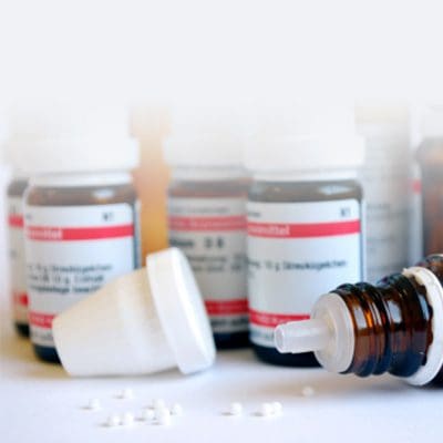 Vor Fläschchen mit homöopathischen Mitteln liegt eine offene Flasche mit einzelnen Globuli.